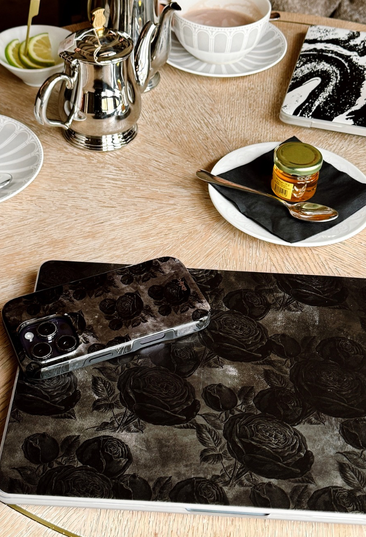 Icon featuring a stylishly arranged table with vintage coffee and tea pots, alongside a MacBook and phone displaying coordinated dark floral cases, emphasizing a 'matchy matchy' aesthetic."